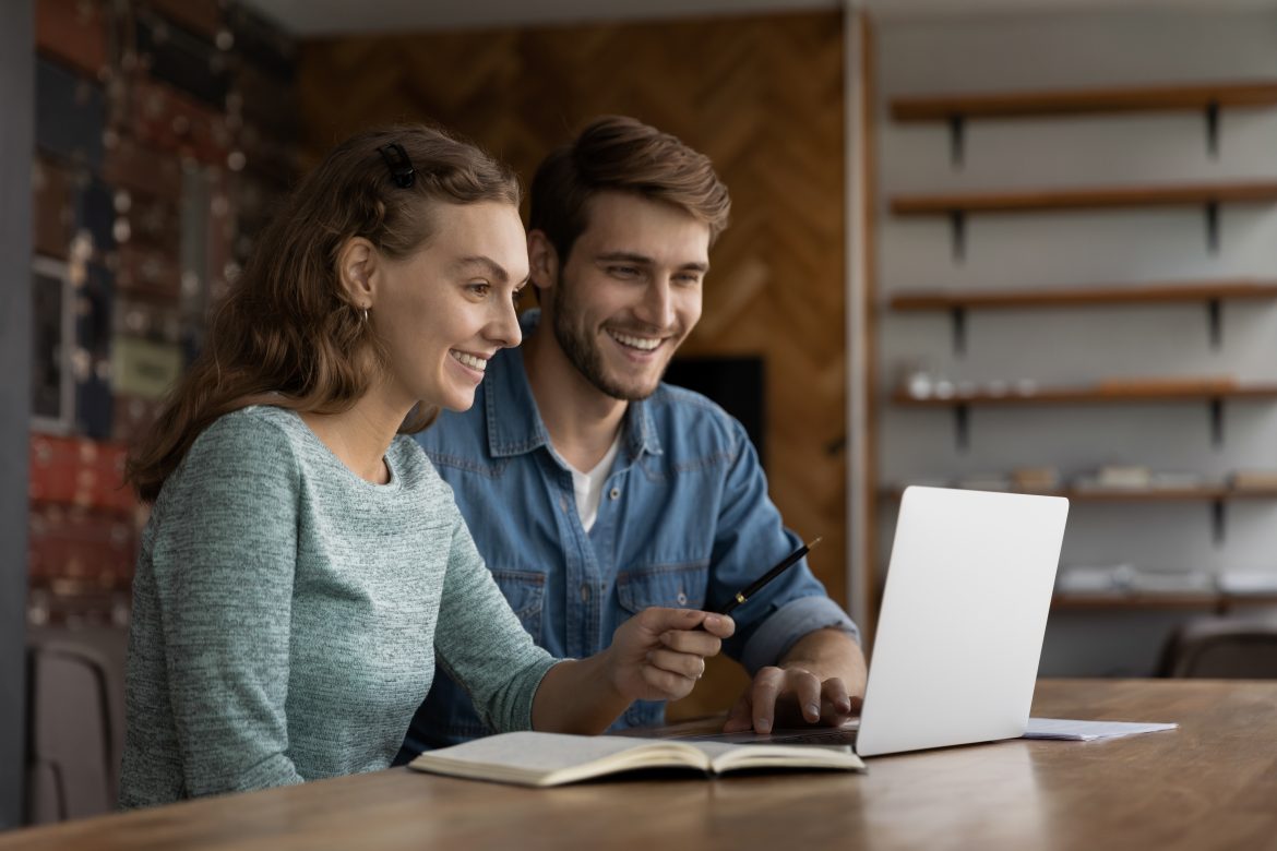 Happy diverse colleagues work on laptop at workplace